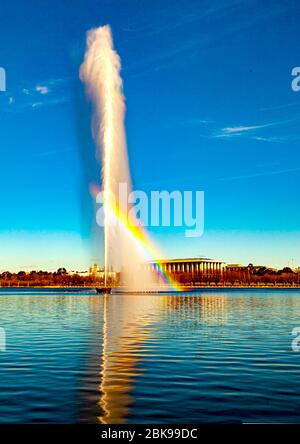 Regenbogen durch Captain Cook Memorial Wasserstrahl auf dem Lake Burley Griffin in Canberra, Australiens Landeshauptstadt mit Nationalbibliothek im Hintergrund Stockfoto