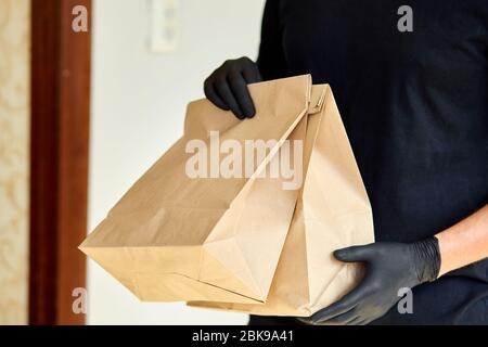 Kurier in schwarzen halten gehen Box Lebensmittel, Lieferservice, Takeaway Restaurants Lebensmittel Lieferung nach Hause Tür. Bleiben Sie zu Hause sicher lebt von Coronavirus COVID-1 Stockfoto