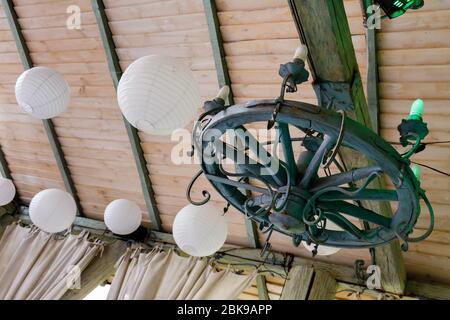 Weiße Kugeln und ein Holzrad mit Kerzenlampen hängen an der Decke. Rustikale Dekoration des Restaurants. Stockfoto