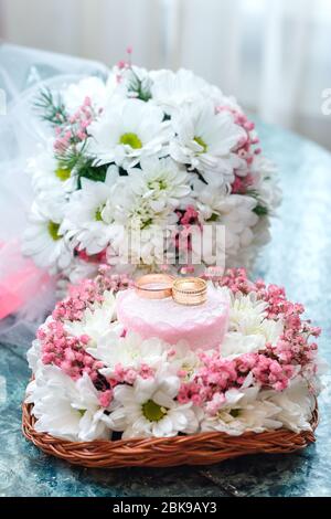 Zwei goldene Eheringe auf schönem weißen und rosa Bouquet in rustikalem Korbflecht. Nahaufnahme. Stockfoto