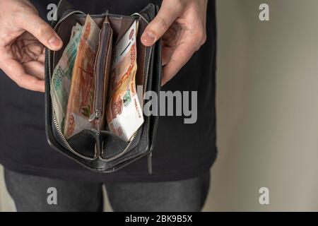 Ein Mann mit einer schwarzen Brieftasche voller russisches Geld. In einer schwarzen Brieftasche, Banknoten sind meist 5,000 Rubel pro Stück. Gehalt und Rente erhöht, Leistungen Stockfoto