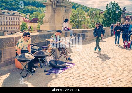 Prag, Tschechische Republik, 13. Mai 2019: Straßenmusiker spielen ihre Hang Drum-Instrumente und der Mensch tanzt auf der kopfsteingepflasterten Fußgängerzone Karlsbrücke Karluv am meisten über der Moldau Stockfoto