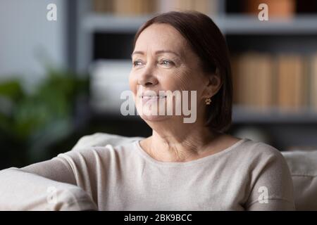 Verträumt lächelnde Frau mittleren Alters, die über gute Zukunft denkt Stockfoto