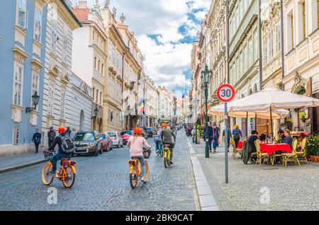 Prag, Tschechische Republik, 13. Mai 2019: Menschen Touristen fahren Fahrräder Fahrräder auf Kopfsteinpflaster Straße in der alten historischen Innenstadt mit Straßenrestaurants und barocken Gebäuden, Böhmen Stockfoto