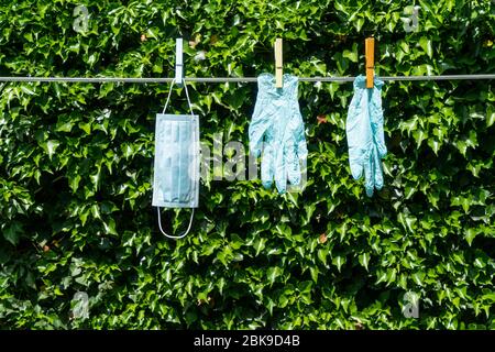 Eine Maske und ein Paar Handschuhe hängen an einem Draht im Garten Stockfoto