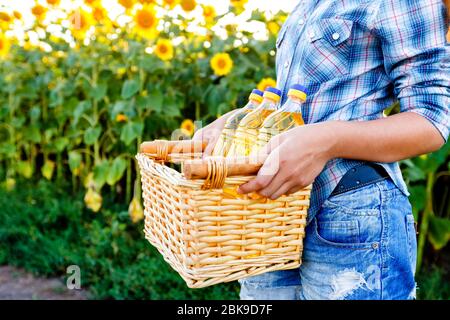 Weidenkorb mit drei Flaschen Sonnenblumenöl in den Händen der Mädchen Stockfoto