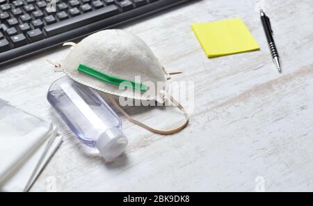 Staubmaske zum Schutz von Gesicht und Flasche Handdesinfektionsmittel auf einem Schreibtisch neben der Tastatur und gelbem Notizpapier mit einem Stift Stockfoto