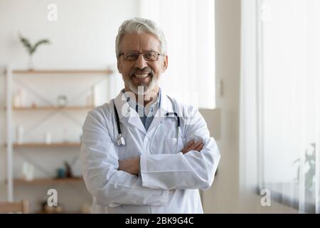 Glücklich alt professionellen Arzt stehend Arme gekreuzt Blick auf Kamera Stockfoto