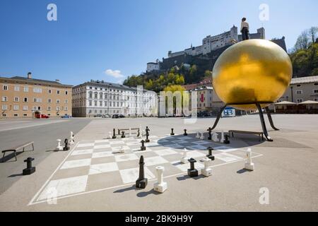 Leere Plätze wegen der Coronavirus-Pandemie, Kapitelplatz mit Goldball-Statue Salzburg und verlassene Schachspielgruppe, Salzburg, Österreich Stockfoto