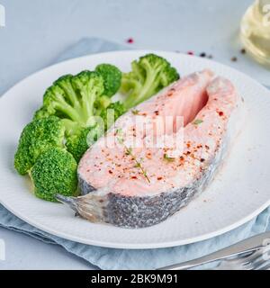 Dampflachs, Brokkoli, Paläo, Keto oder fodmap Diät. Weiße Platte auf blauem Tisch, Seitenansicht Stockfoto