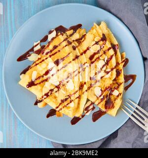 Zwei Pfannkuchen mit Schokoladensirup, Mandelflocken auf Platte, Honig fließt aus Löffel, Draufsicht, Makro Stockfoto
