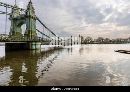 Locksdown London: Eine hohe Flut überflutet den Schleppweg um die Hammersmith Bridge und steigt die Bastionen hinauf. Die Wanderer auf der Brücke sind gestream Stockfoto