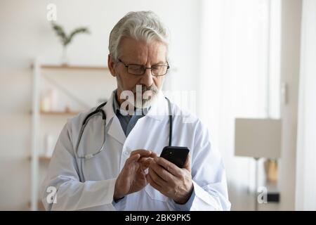 Senior männlichen Arzt hält Smartphone mit medizinischen Anwendungen Stockfoto