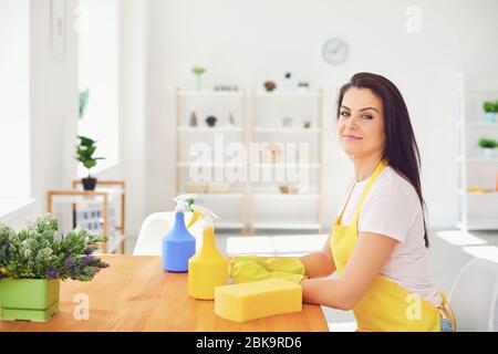 Glückliche junge Frau reinigt das Zimmer im Haus. Mädchen waschen in Handschuhen, während auf dem Boden lächelnd lächelnd sitzen. Stockfoto