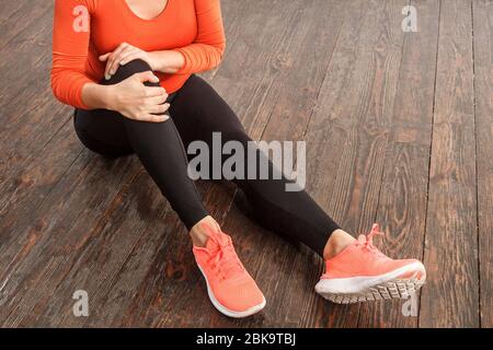 Fit Frau in engen Sportbekleidung hält schmerzhafte Knie sitzt auf dem Boden zu Hause Fitness-Studio, leiden Muskelbelastung, Verstauchung Bänder oder Gelenkverletzungen, Gesundheit pro Stockfoto