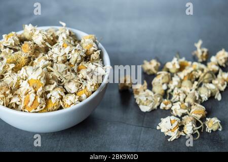 Getrockneter Kamillentee in weißer Porzellanschale auf Stein, Betonuntergrund. Trockene, biologische, gesunde und entspannende Kräuter. Stockfoto