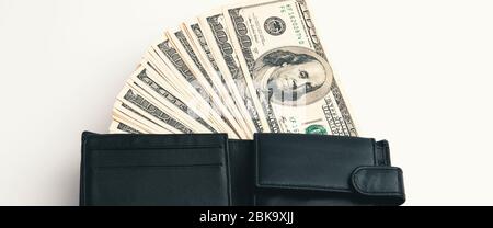 Eine schwarze Geldbörse mit Dollar darin auf weißem Hintergrund. Die hundert-Dollar-Rechnungen sind halb aus und angeordnet in einem Ventilator. Kontrastvolles Farbbild. Stockfoto