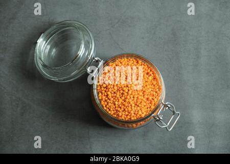 Rote Linse im Glas auf Stein, Betonhintergrund. Gesunde, biologische und köstliche Rohkorienprodukte. Draufsicht, flaches Lay. Stockfoto