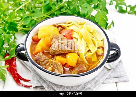 Zentralasiatisches Nationalgericht Lagman aus Fleisch, Nudeln und Gemüse in der Schüssel auf einer Serviette, Knoblauch, Petersilie auf weißem Holzbrett Stockfoto