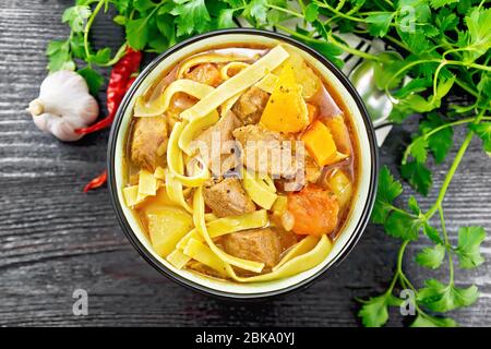 Zentralasiatisches Nationalgericht Lagman aus Fleisch, Nudeln und Gemüse in der Schüssel auf der Serviette, Knoblauch, Petersilie auf dunklem Holzbrett von oben Stockfoto