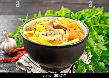 Zentralasiatisches Nationalgericht Lagman von Fleisch, Nudeln und Gemüse in der Schüssel auf einem Handtuch, Knoblauch, Petersilie auf Holzbrett Hintergrund Stockfoto