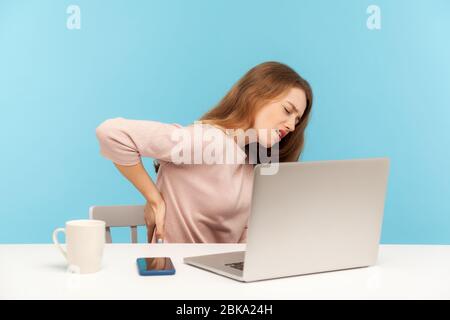 Ermüdete ungesunde Frau, Büroangestellte, am Arbeitsplatz sitzend, sich unwohl mit Rückenschmerzen fühlend, verletzte steife Muskeln und Krämpfe durch sitzende Lebenskraft Stockfoto