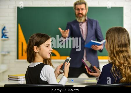 Pupille Trägt Uniform. Kleine Schüler studieren und lesen. Hausaufgaben schreiben und lesen. Kinder Mädchen und Lehrer Mann. Grundlehrer, Der Im Klassenzimmer Unterstützung Gibt. Analyse der Strategie. Stockfoto