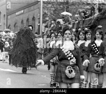 Die jährliche Knutsford Royal May Day Prozession im Jahr 1976 in Knutsford, Cheshire, England, Großbritannien. Traditionell umfasst es einen Kostümzug von Kindern in historischen oder legendären Kostümen mit Pferdekutschen. Hier marschieren Mädchen in Uniform vor einem grünen Mann oder Jack in the Green. Der Jack in the Green oder Green man ist Teilnehmer an traditionellen englischen Maifeierlichkeiten und anderen Maifeiern, der einen großen, mit Laub bedeckten Rahmen trägt. Stockfoto