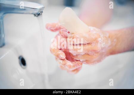 Eine Person wäscht ihre Hände mit weißer, sanfter Seife, die gut schäumt, und das Leitungswasser fließt in das Waschbecken. Zärtlichkeit und Hygiene. Stockfoto