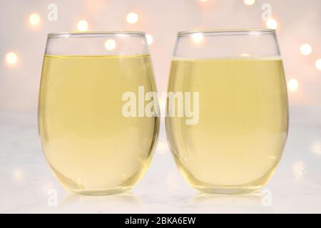 Zwei Weingläser ohne Stielfüllung mit Weißwein auf Marmorgrund. Weiße Lichter leuchten im Hintergrund. Stockfoto