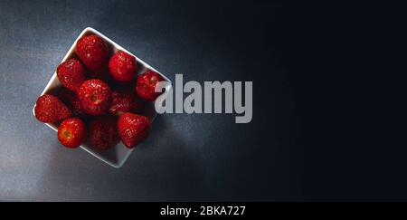 Flatlay eine Schüssel mit frischen Erdbeeren, dunkel und stimmungsvoll beleuchtet mit harschen schwarzen Hintergrund Draufsicht modernes Bild. Kopierbereich Stockfoto