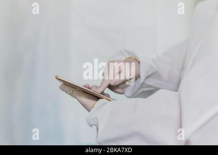 Arzt oder Krankenschwester, die einen Schutzanzug und Handschuhe tragen und dabei die Technologie nutzen, um Daten über das schnell verbreitete Coronavirus auf einem Tablet zu analysieren Stockfoto