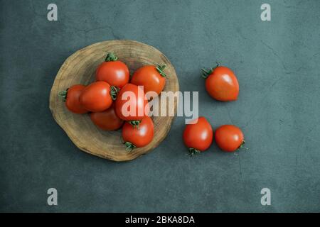 Rote kleine Kirschtomaten in Holzservierteller auf Stein, Betonhintergrund. Frisch geerntetes leckeres, gesundes und biologisches Gemüse. Flaches Lay Stockfoto
