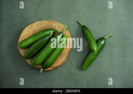 Bio Mini Gurke auf Holzservierung Teller bereit zu essen. Frisch geerntet gesundes und leckeres Essen. Draufsicht, flaches Lay. Stockfoto