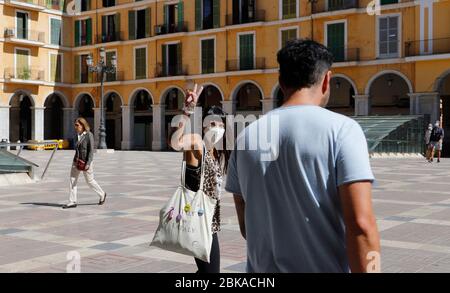 Palma, Spanien. Mai 2020. Die Leute gehen durch die Plaza Mayor im Stadtzentrum, eine junge Frau mit Mundschutz macht das Siegeszeichen. Nach fast 50 Tagen strikter Quarantäne während der Corona-Krise in ihren Häusern werden Menschen innerhalb der ihnen zugewiesenen Fristen und unter Einhaltung der Sicherheitsabstände an die freie Luft entlassen. Kredit: Clara Margais/dpa/Alamy Live News Stockfoto