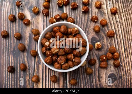 Rohe Haselnuss auf altem Holztisch. Geröstete Haselnüsse in weißer Schale und verstreute Haselnüsse. Stockfoto