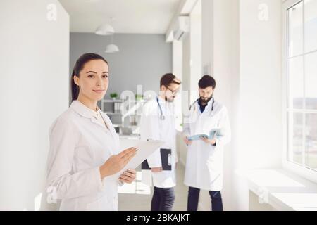 Eine Praktizierende Ärztin mit Stethoskop lächelt vor dem Hintergrund eines Arztes in der Klinik. Stockfoto