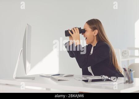 Geschäftsfrau, die Computer-Monitor durch Fernglas betrachtet Stockfoto