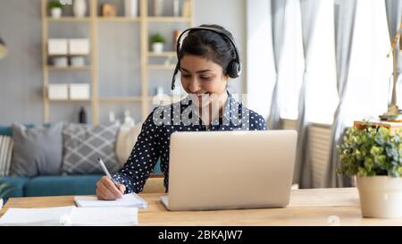 Lächelnde hindu-Frau, die online studiert, am Schreibtisch mit Computer sitzt. Stockfoto