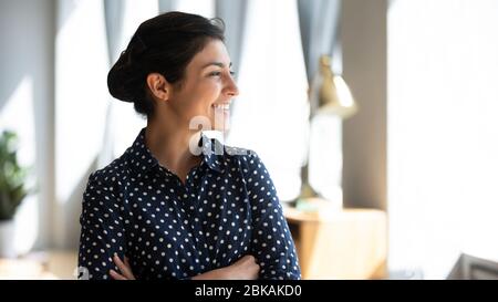 Glücklich junge indische Mädchen mit gefalteten Armen zu Hause stehen, Blick auf Fenster. Stockfoto