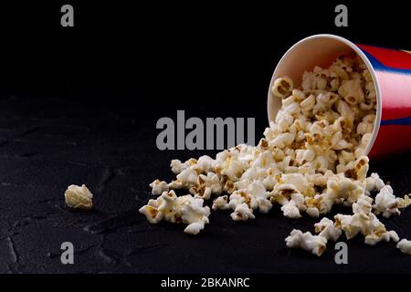 Umgekippte Tasse mit schmackhaftem Popcorn auf dunklem Hintergrund. Stockfoto