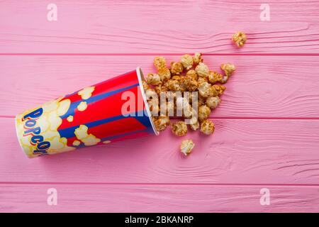 Frittieren Sie Popcorn aus umgekipptem Eimer auf rosa Holzhintergrund. Stockfoto