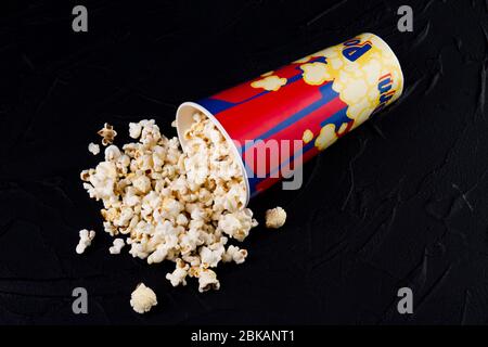 Leckeres Popcorn aus einem umgekippten Kasten dunklen Hintergrund verschüttet. Stockfoto