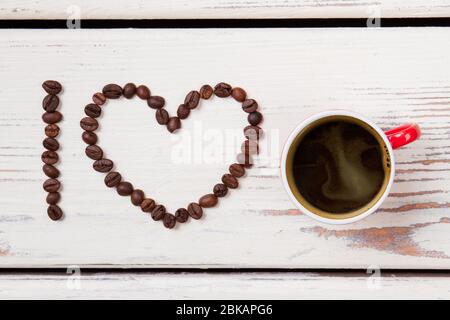 Rote Tasse Kaffee und Bohnen in Herzform angeordnet. Stockfoto