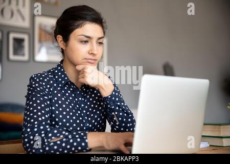 Nachdenkliche junge indische Frau, die auf Computerbildschirm schaut. Stockfoto