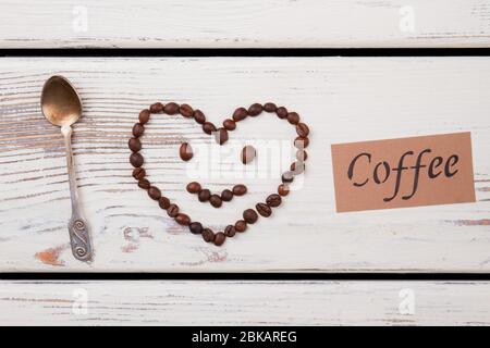 Herz Smiley aus Kaffeebohnen und Teelöffel auf Holz. Stockfoto