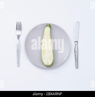 Die Hälfte der Zucchini auf den Teller geschnitten. Kreatives Konzept Frische Zucchini auf isoliertem Hintergrund. Stockfoto