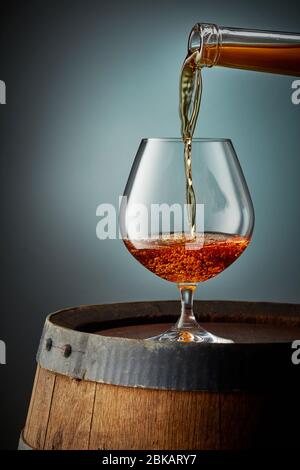 cognac goss in Glas auf alten Holzfass Stockfoto