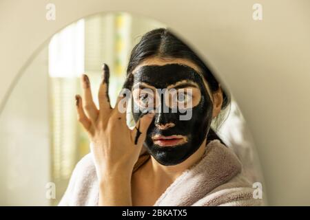 Eine junge Millennial Frau weiblich Anwendung einer Detox schwarze Kohle Peel off Gesichtsmaske Schönheitsbehandlung im Hause Bad London England UK Stockfoto