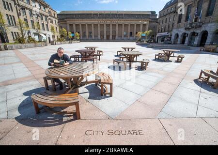 Ein Mann liest sein Buch auf einem verlassenen City Square im Stadtzentrum von Dundee, während Großbritannien weiterhin in der Blockierung ist, um die Ausbreitung des Coronavirus einzudämmen. Stockfoto